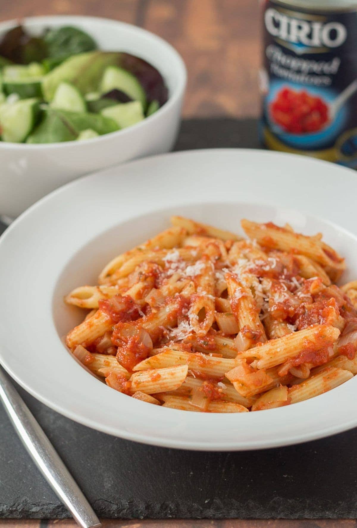 pasta arrabiata serving in white bowl with spoon nearby.
