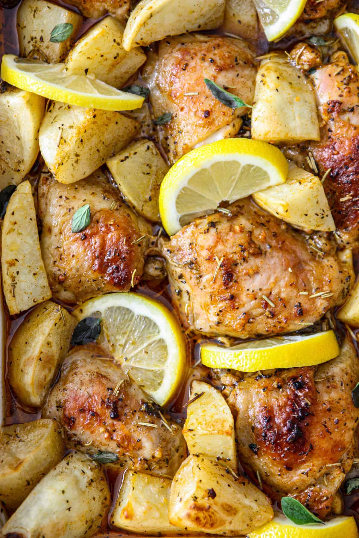 Greek lemon chicken with potatoes and lemon slices in baking dish, close-up.