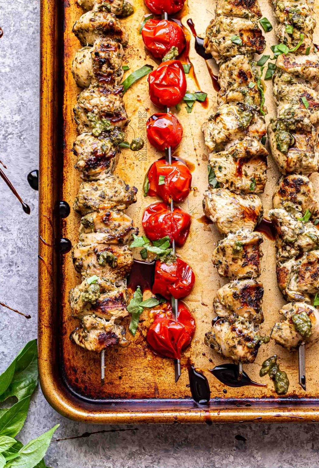 grilled pesto chicken and tomato skewers on tray drizzled with balsamic glaze.