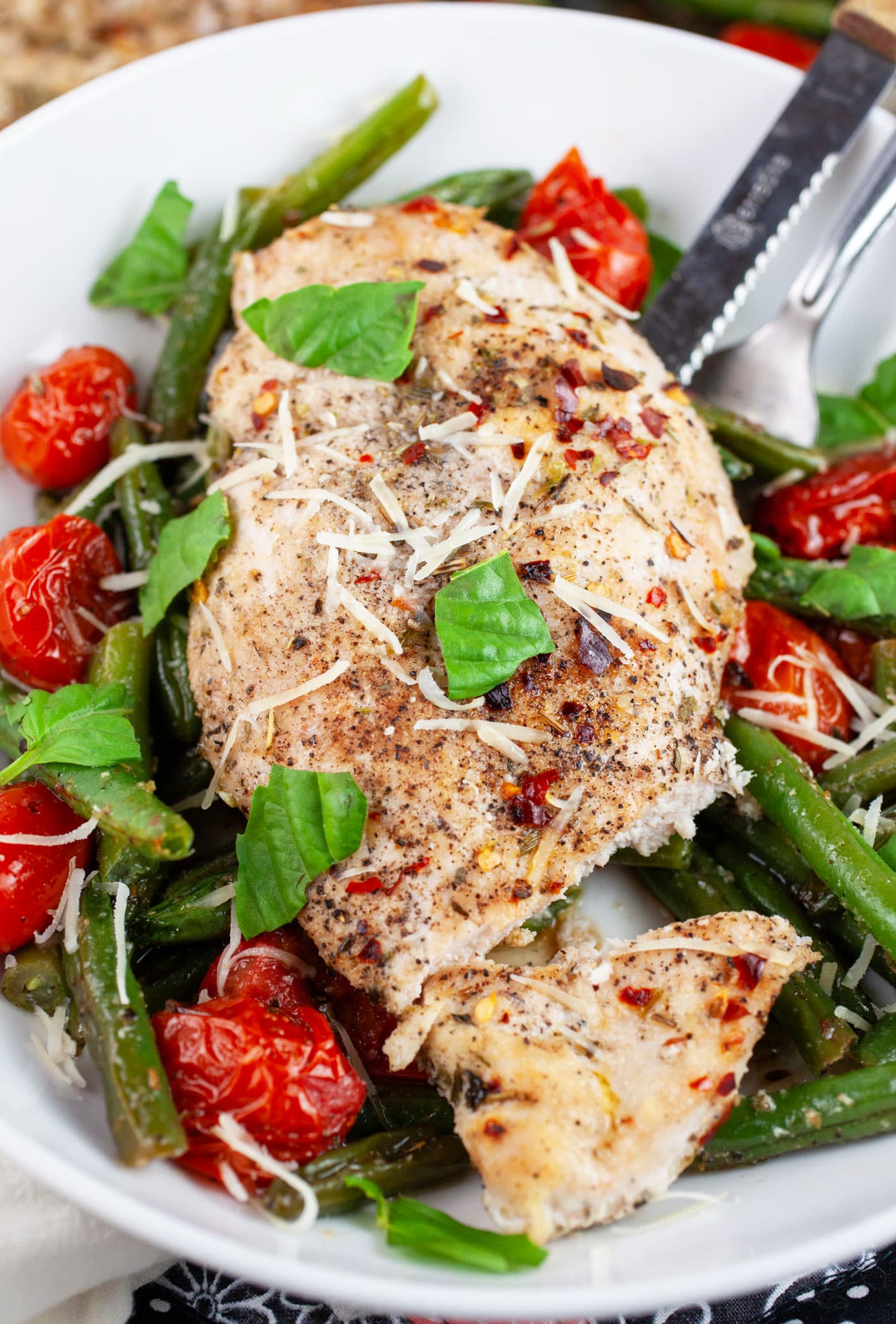 Italian chicken with roasted tomatoes and green beans on white plate.