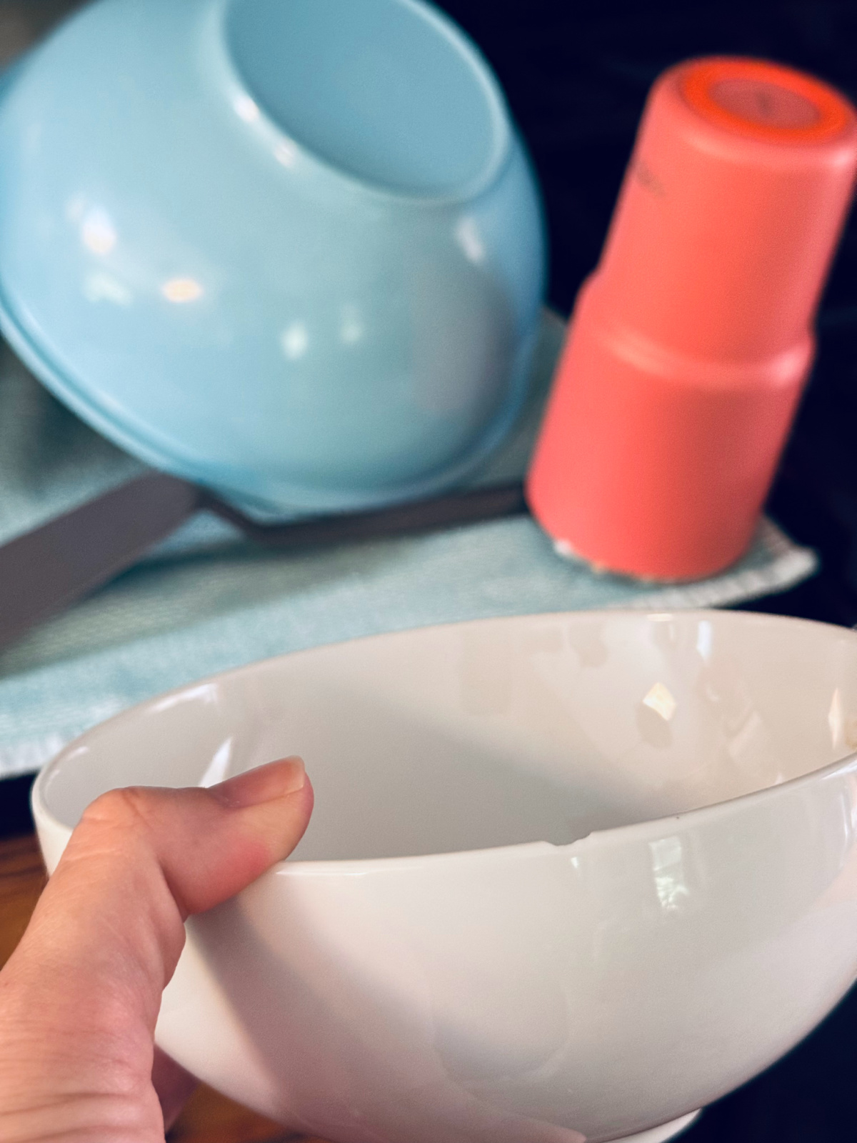chipped white bowl in focus with dry dishes in background on counter.