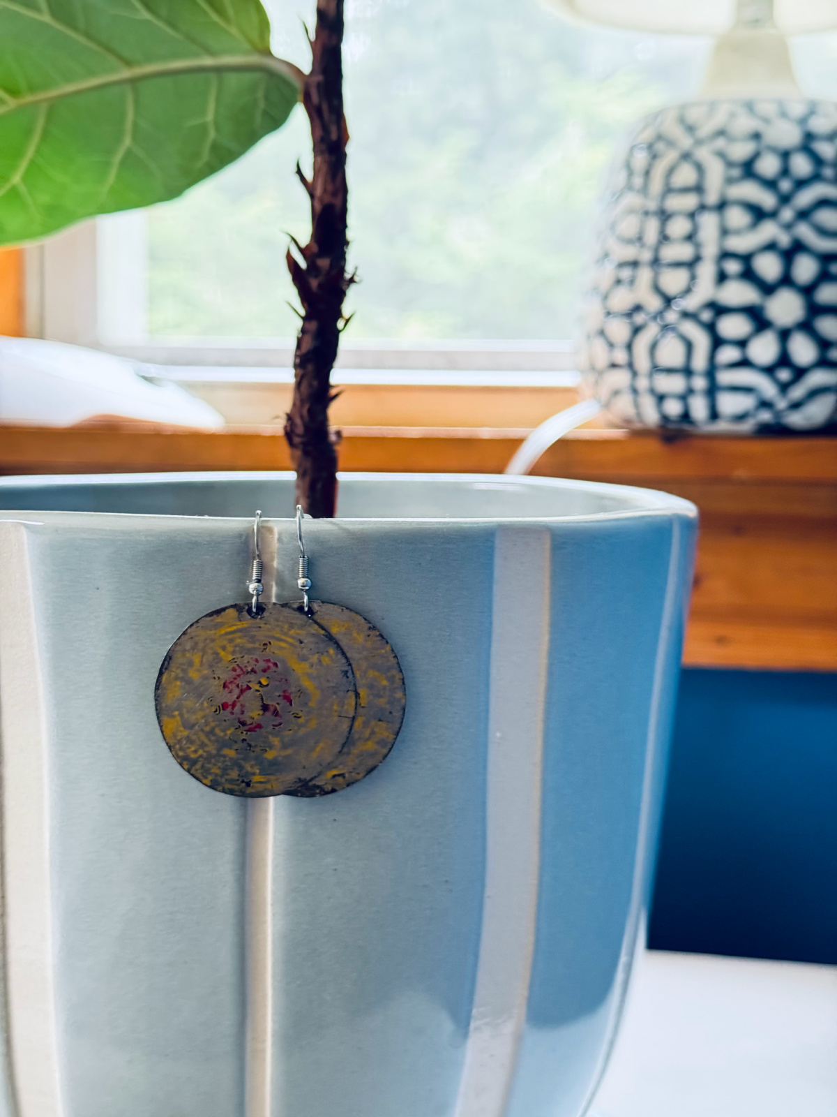 round earrings hanging on blue and white striped planter.