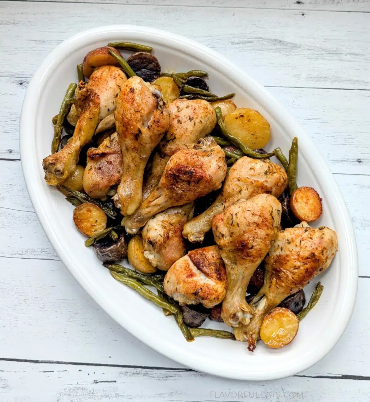 white platter with chicken drumsticks, roasted potatoes and green beans.