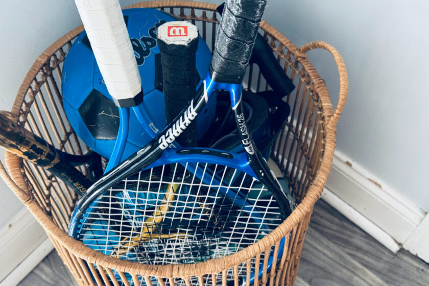 tennis rackets and soccer ball in basket, representing July decluttering.